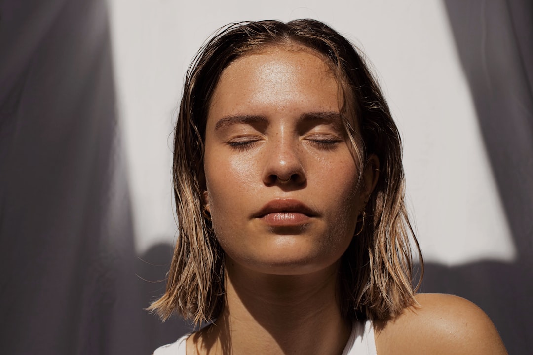 A young woman with her eyes closed is lit by sunlight and shadows