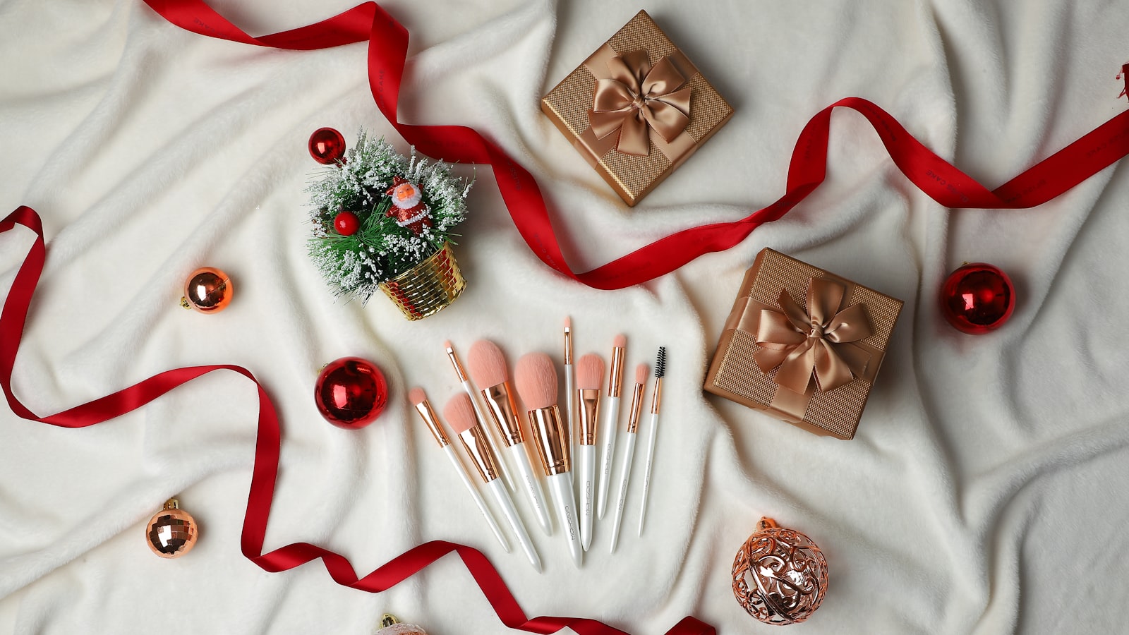Top-down view of makeup brushes, gift boxes, and holiday ornaments on a white blanket