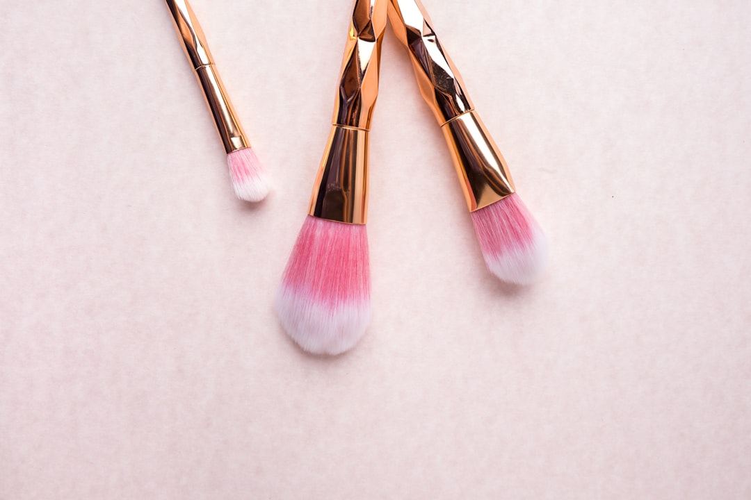 Three gold-handled brushes with pink bristles on a pale pink surface