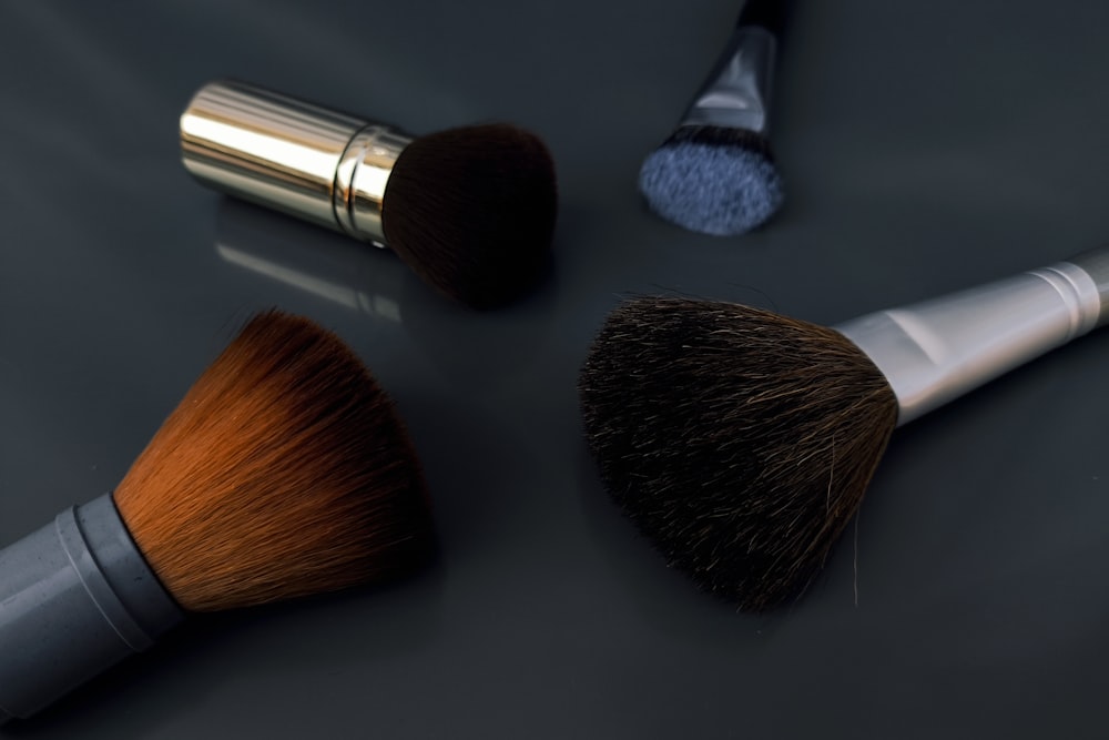 Four cosmetic brushes with different colored bristles are scattered on a dark gray surface