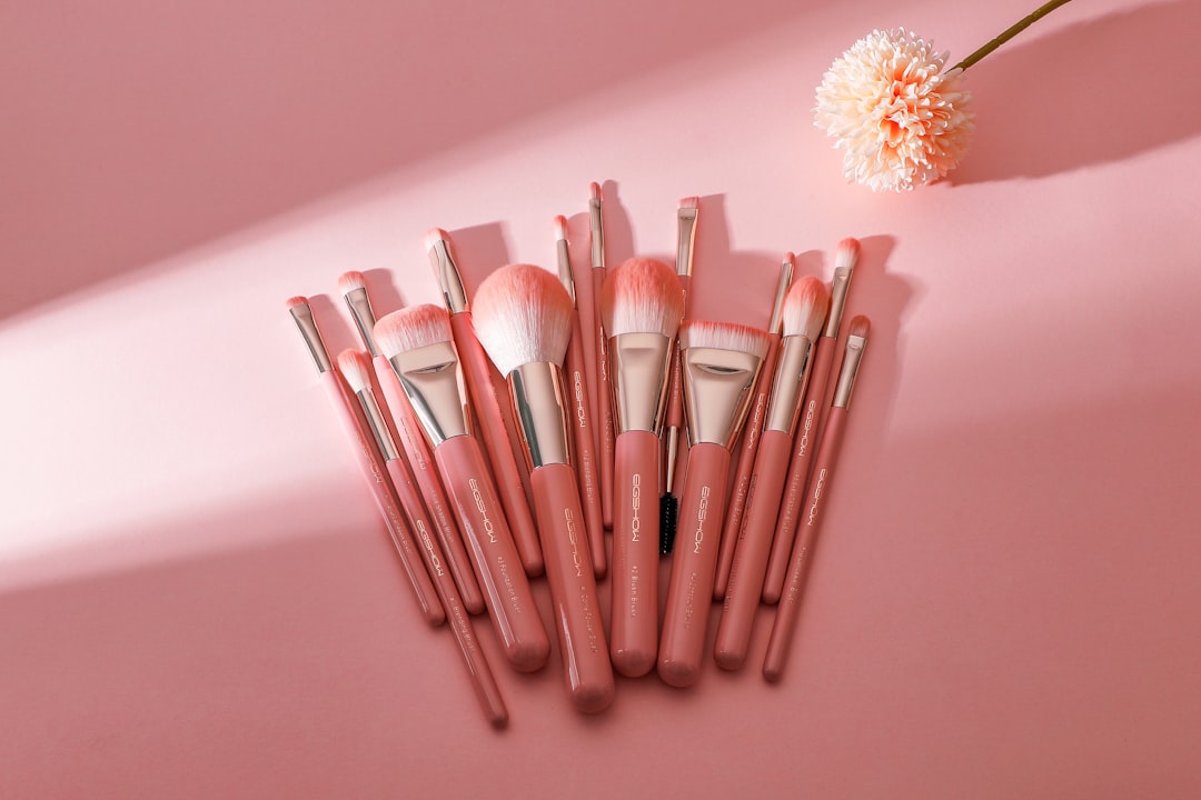 Set of pink-handled makeup brushes fanned out on a pink background beside a flower