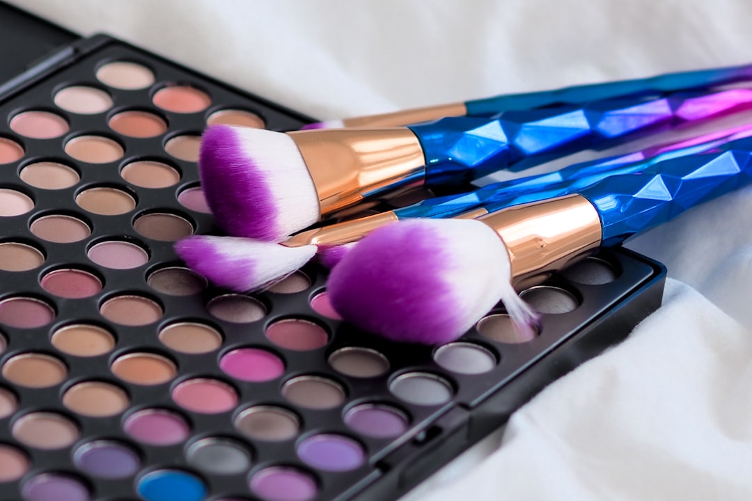 Two brushes with purple bristles and blue handles resting on an open eyeshadow palette