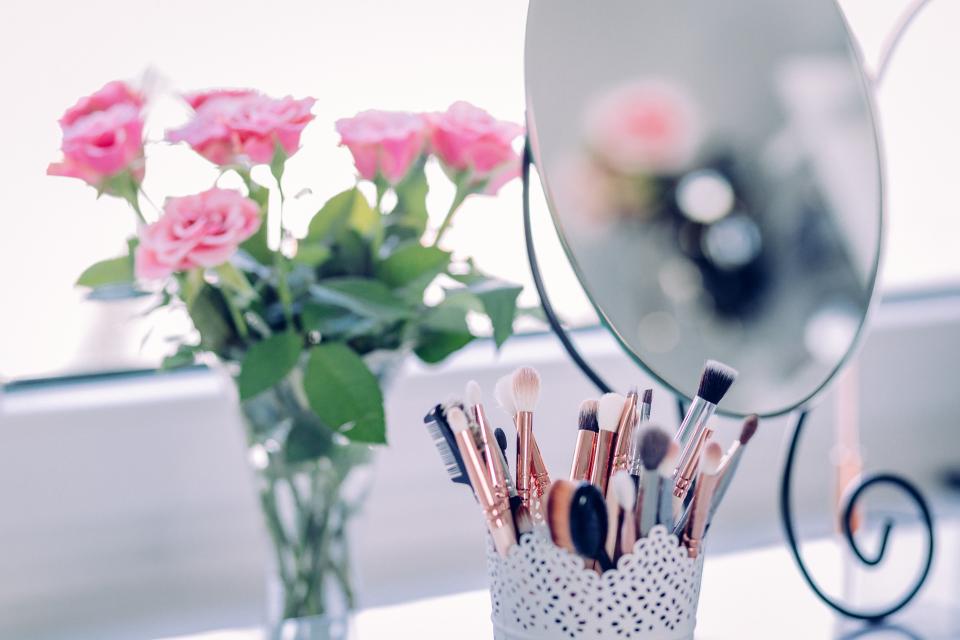 A bouquet of pink roses and a makeup brush holder sit next to a round mirror