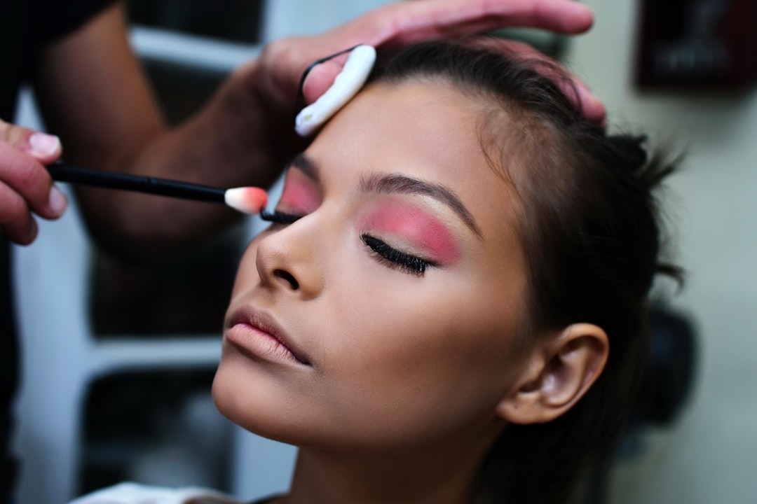 Makeup artist applying pink eyeshadow to a model's closed eye with a small brush