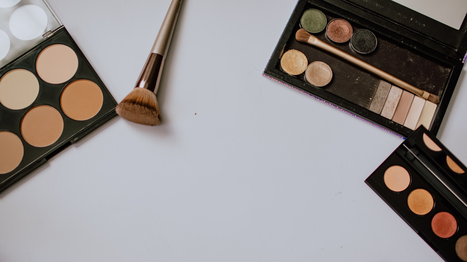 Eyeshadow and contour palettes with makeup brushes arranged on a white surface
