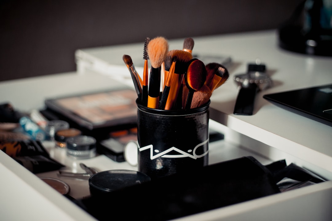 Assorted makeup brushes standing in a pot on a vanity beside palettes