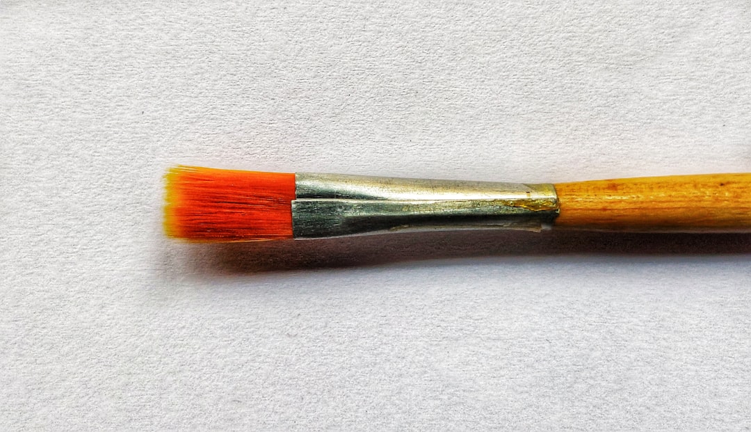 Flat brush with orange bristles resting on white paper