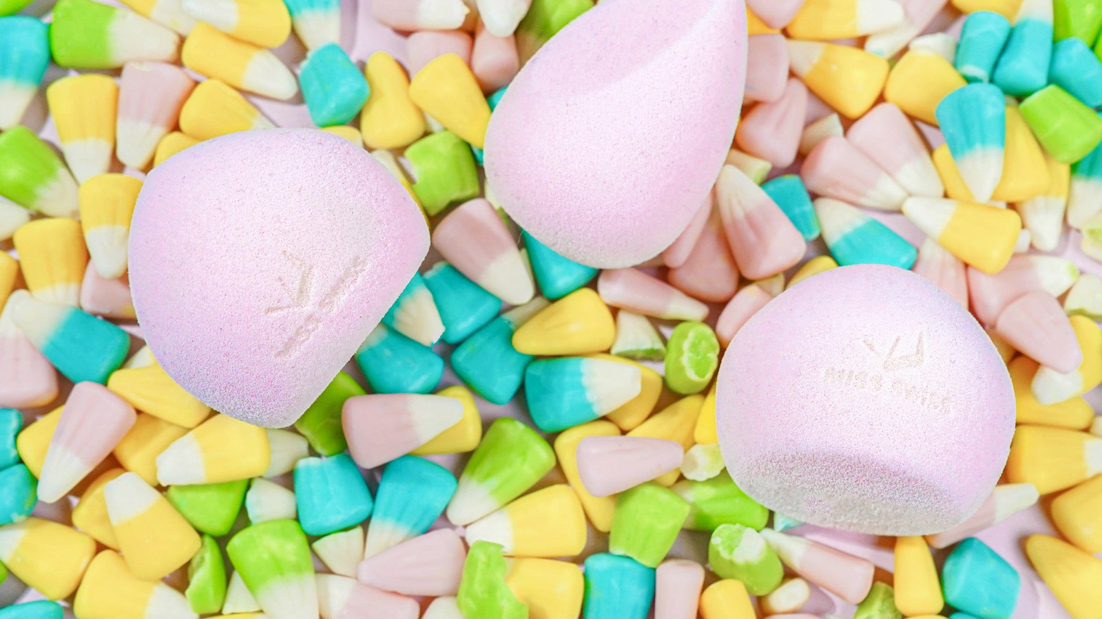 Three pink makeup sponges scattered among a backdrop of colorful candy corn