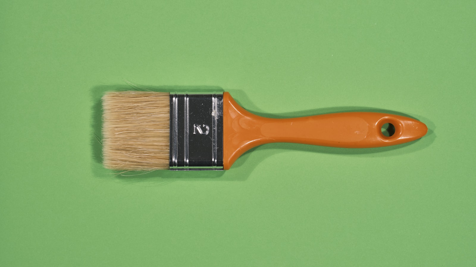 A flat paintbrush with an orange plastic handle on a green background