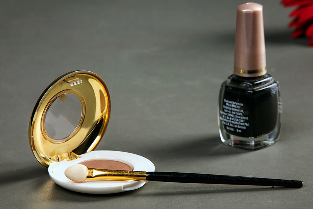 An open powder compact with an applicator brush resting on it and a bottle of dark nail polish nearby