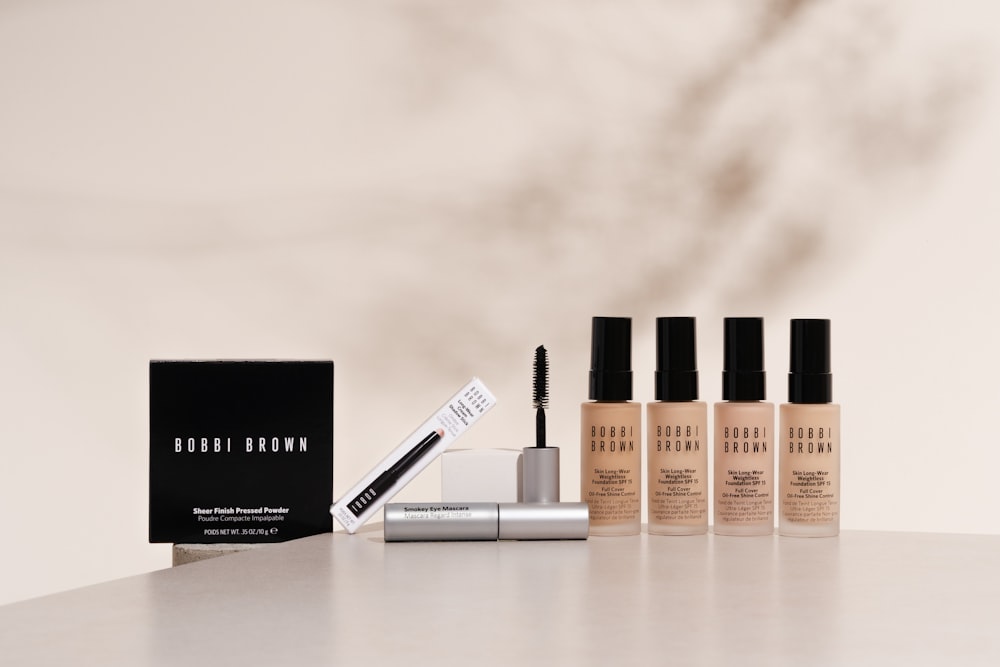 Cosmetics including powder, mascara, and four foundation bottles stand on a surface