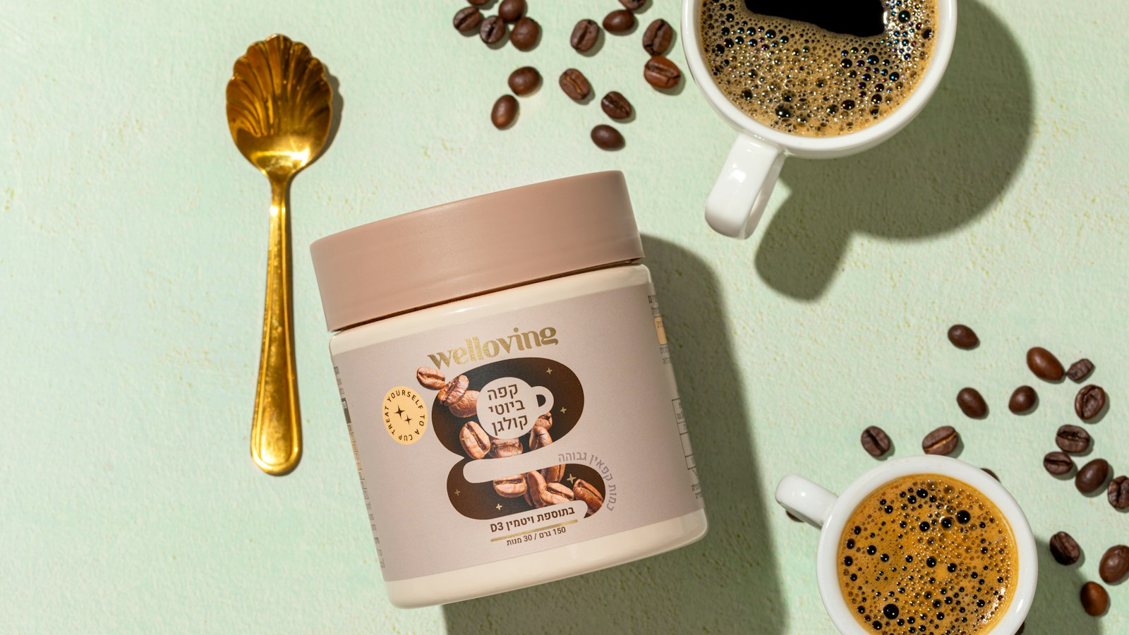 A jar of coffee powder, two cups of coffee, a gold spoon, and scattered coffee beans on a light green surface