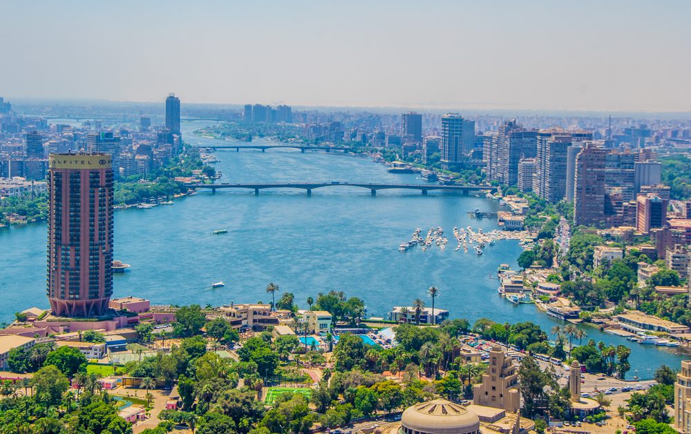 An aerial view of a wide river flowing through a dense city with high-rise buildings and bridges
