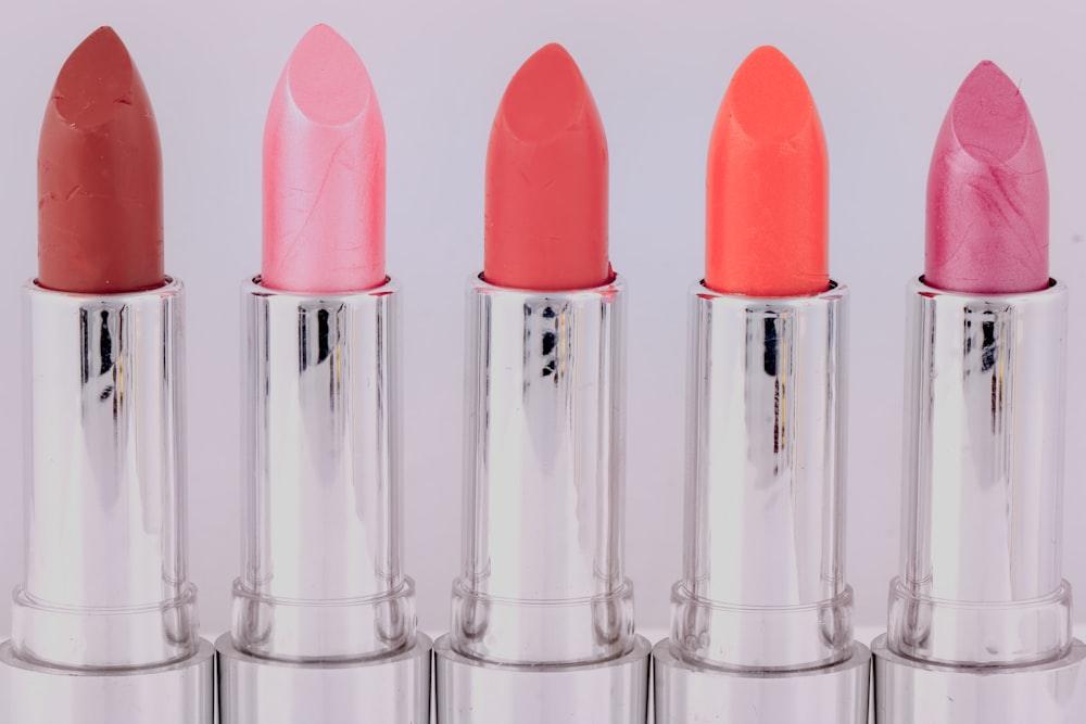 Five open tubes of lipstick in different shades stand in a row against a light background