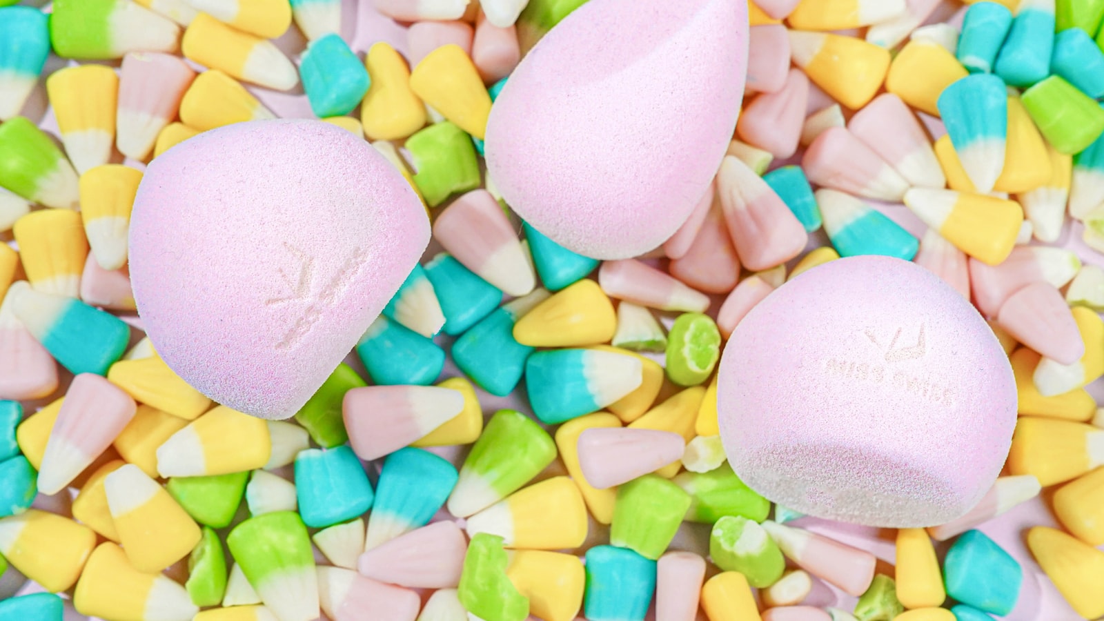 Three pink makeup sponges resting on a bed of multi-colored candy corn