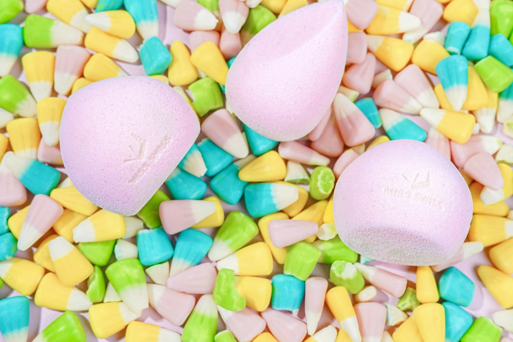 Three pink makeup sponges lie on a pile of multi-colored candy corn
