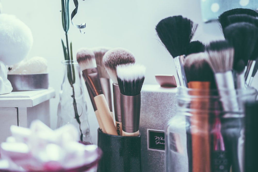 Makeup brushes in holders with a vase and white box in the background