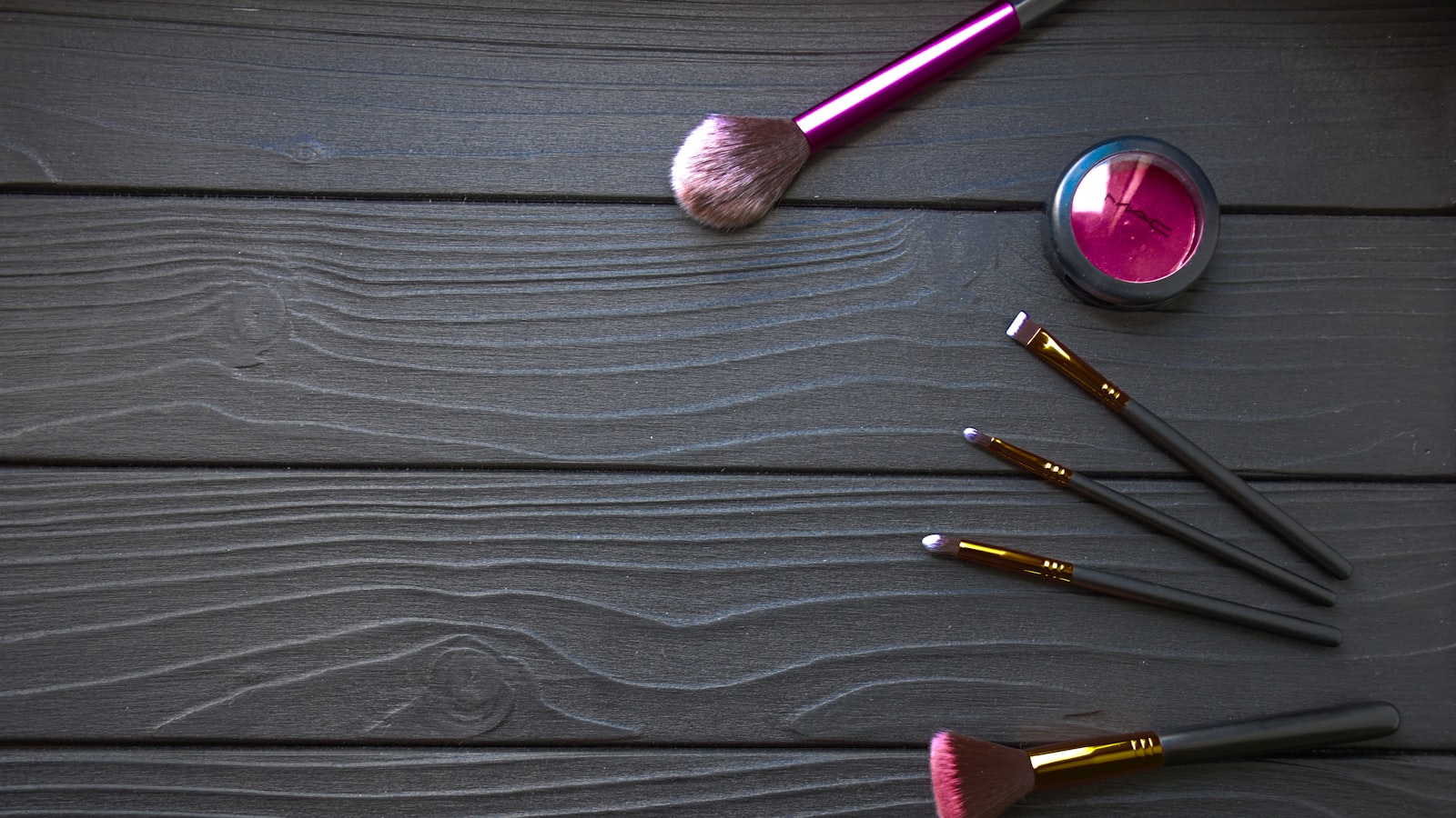 A purple and black makeup palette and five brushes lie on a dark wooden surface