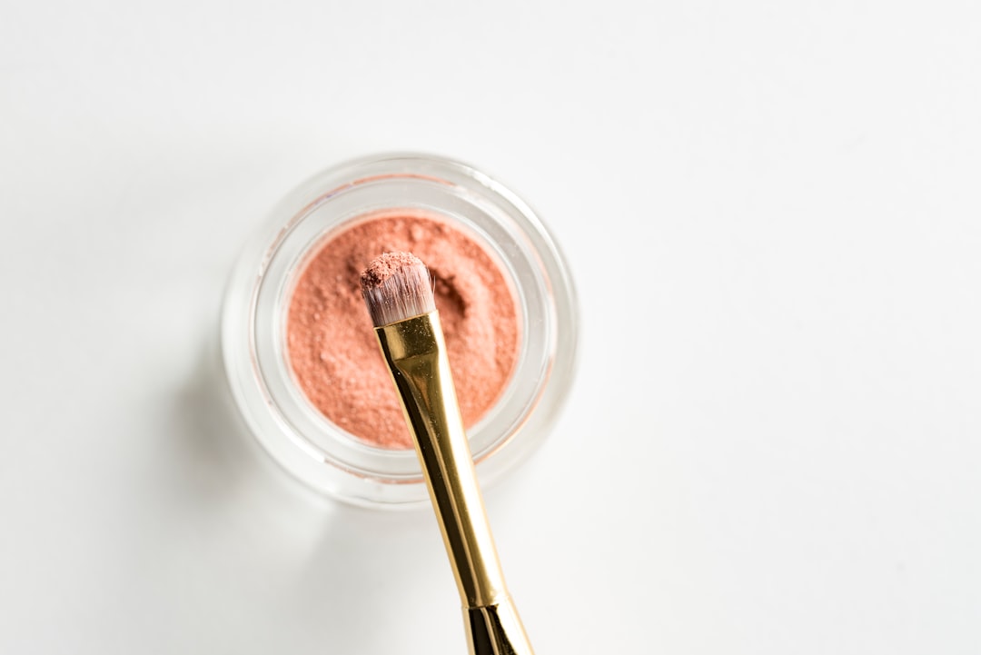 Small gold-handled brush resting on an open jar of loose pink powder