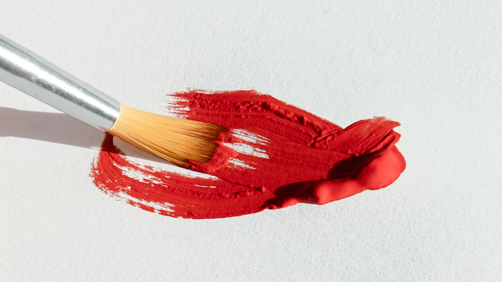 A paintbrush with bright red paint rests on a textured white surface