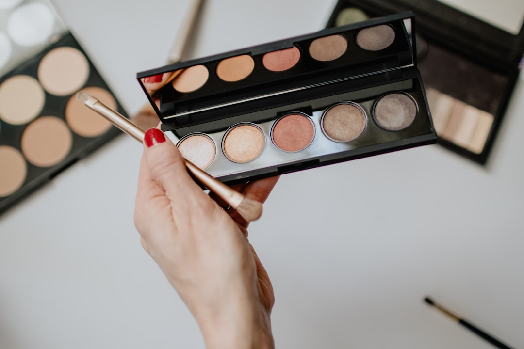A hand holds an open eyeshadow palette with five pans and a small brush