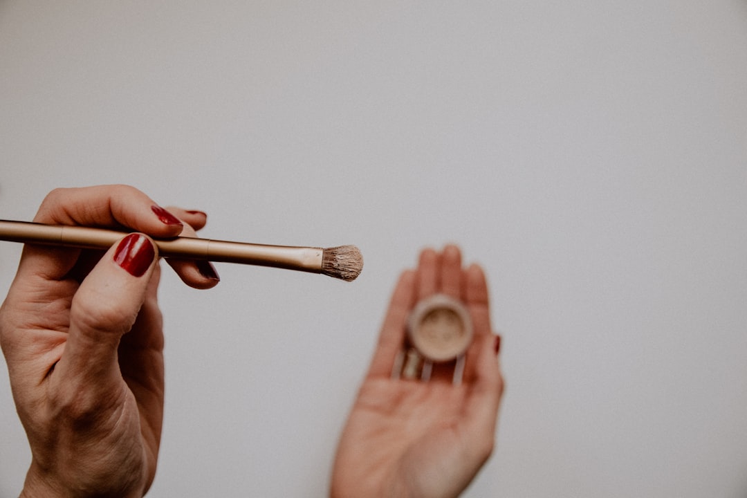 One hand holding a gold makeup brush, the other holding a small pot of powder