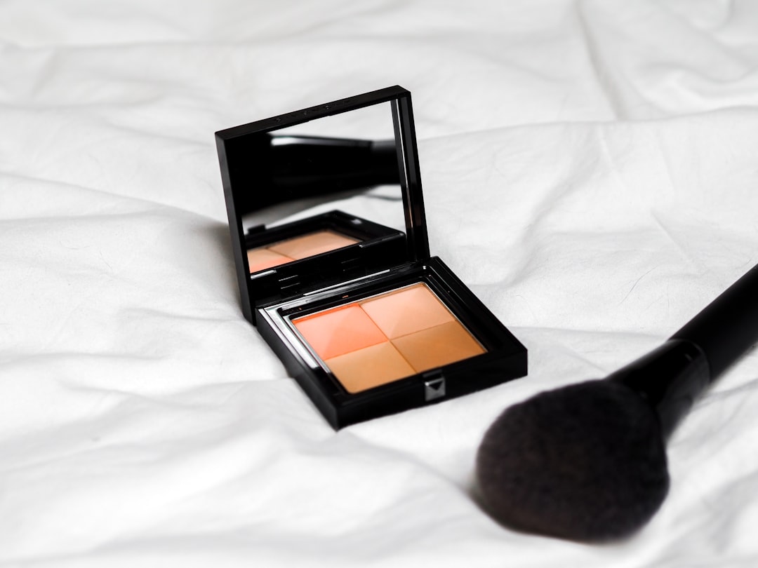 An open makeup compact with a four-color powder pan sits on white fabric next to a makeup brush
