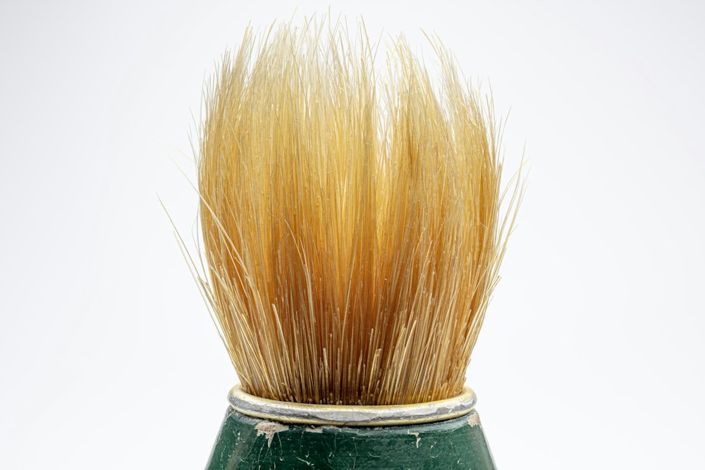 Close-up of golden-brown bristles of a shaving brush in a dark green handle against a white background