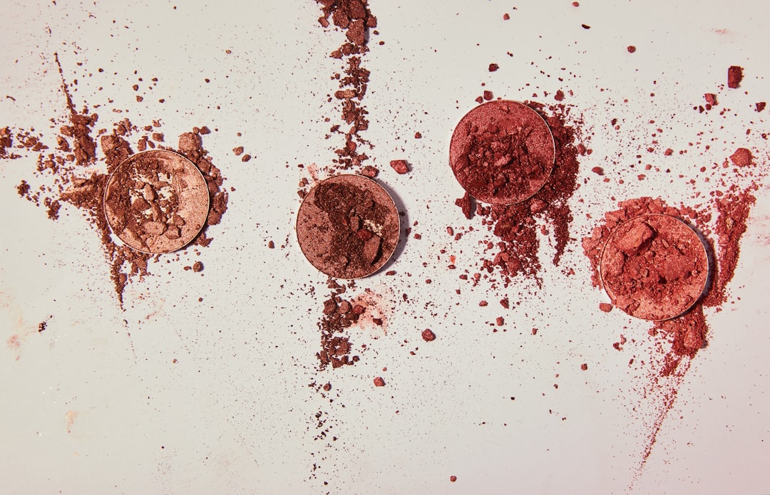 Four crushed eyeshadow pans with scattered powder on a light surface