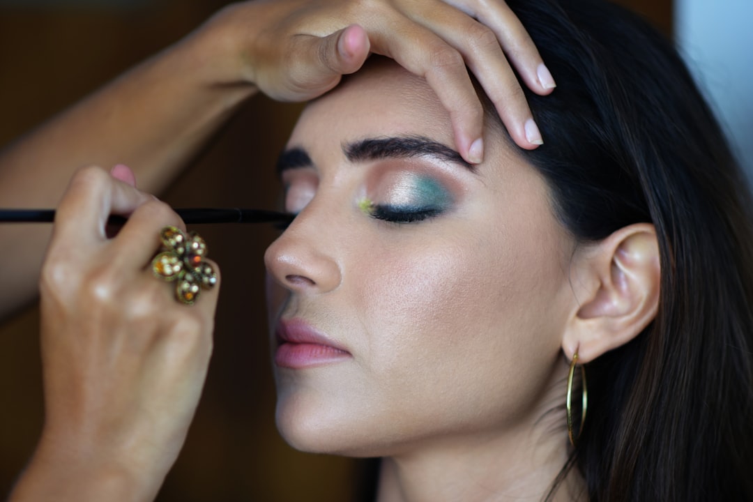 Makeup artist applying eyeliner to a model wearing teal eyeshadow