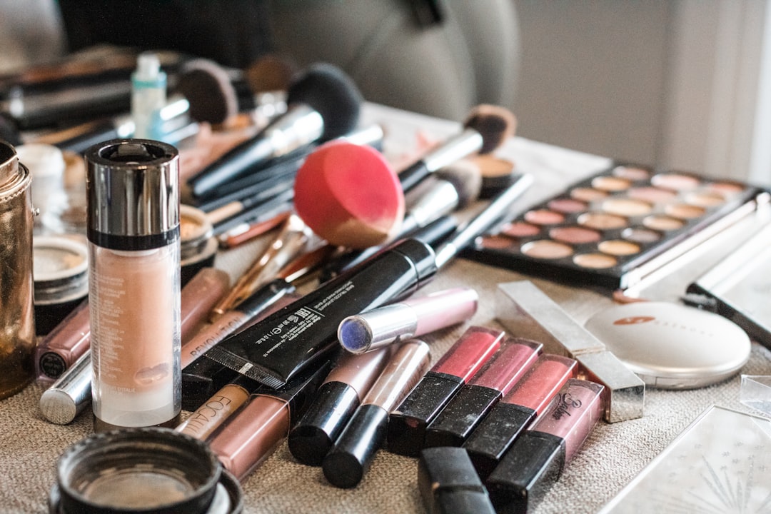 Table covered with makeup products: lipsticks, foundation, a sponge, brushes and an eyeshadow palette