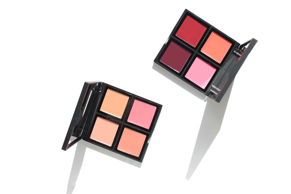 Two open square cosmetic palettes with four colored pans each on a white background