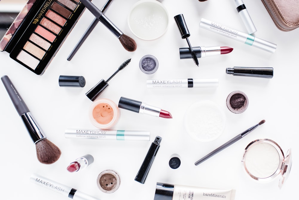 Makeup products and brushes are scattered on a white surface