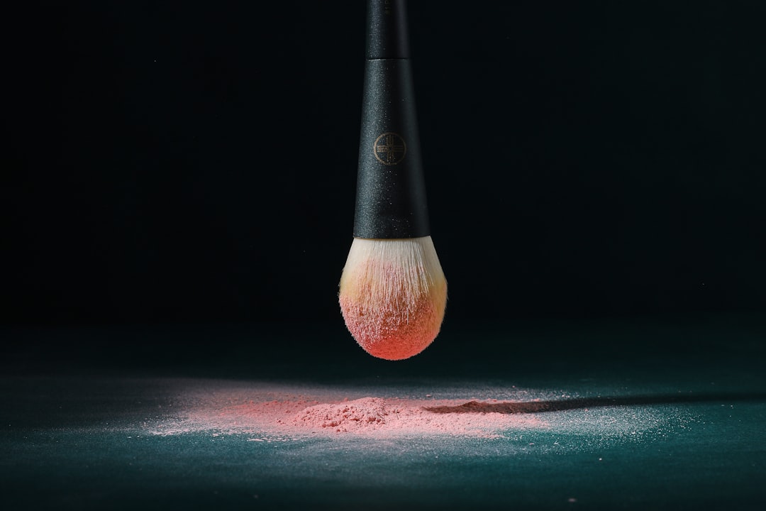A black handled brush with pink powder on its bristles hovers over a dark surface