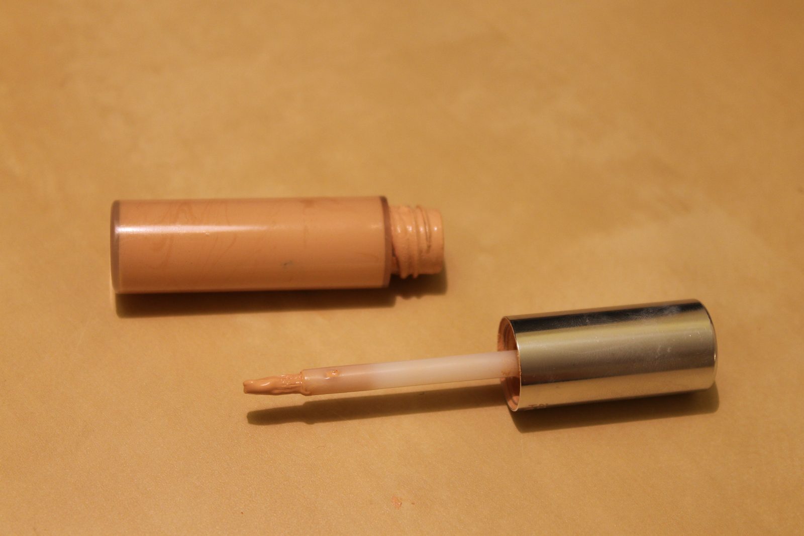 An open tube of liquid makeup and its applicator wand resting on a flat surface