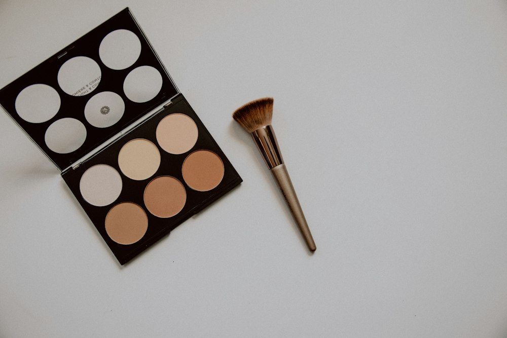 An open makeup palette and a brush lie on a light surface