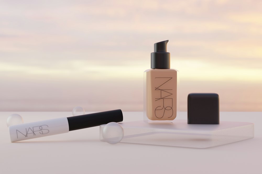 Two NARS cosmetic bottles and glass spheres sit on a platform with a sunset background