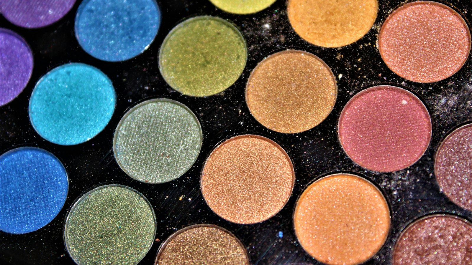 Close-up view of an eyeshadow palette with circular pans in blues, greens, golds, and pinks