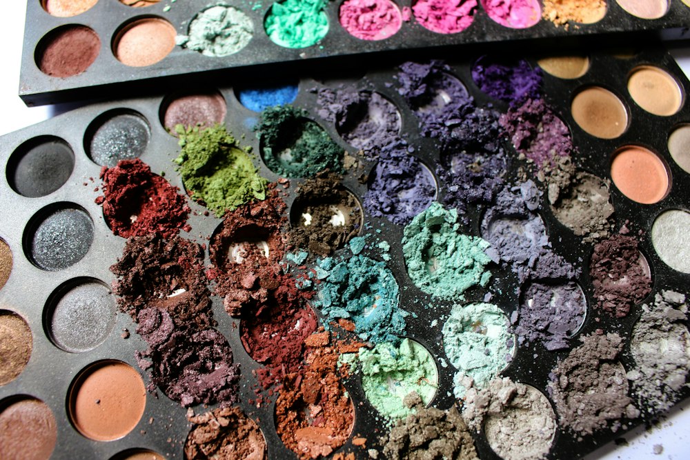 Two used makeup palettes with many crushed and broken eyeshadow colors