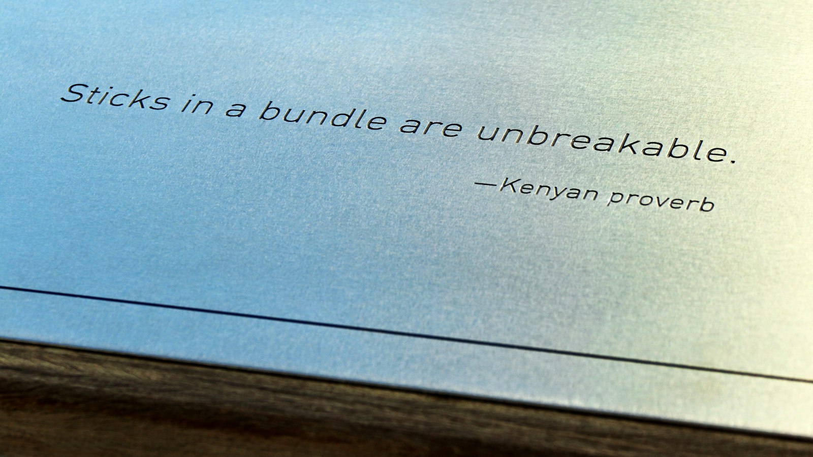 A blue metal plate with the engraved text "Sticks in a bundle are unbreakable.—Kenyan proverb"