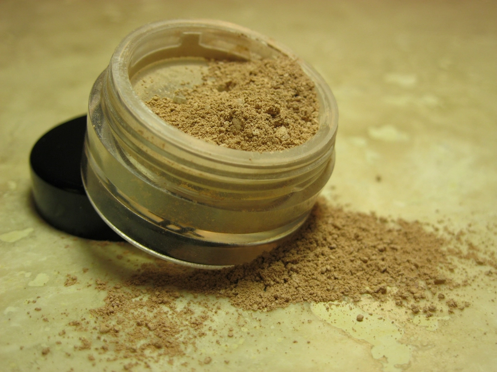 An open, clear plastic jar with a black lid filled with light brown powder, sitting on a speckled counter