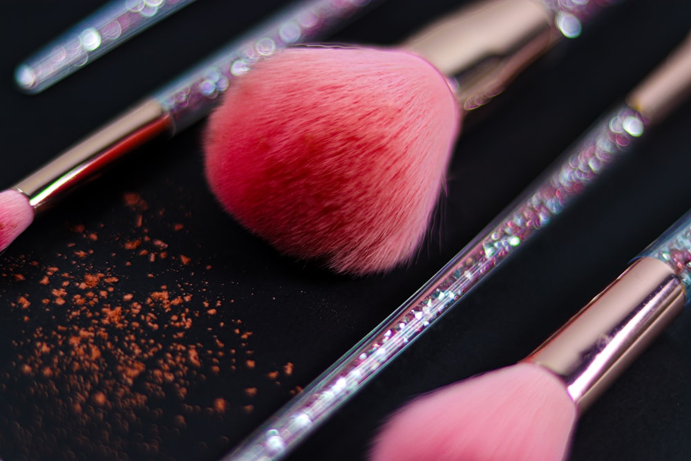 Several pink cosmetic brushes with glitter-filled handles lie on a black surface with scattered pink powder