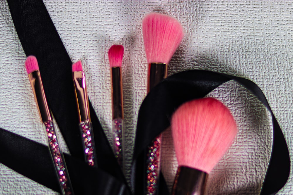 Pink-bristled brushes with glitter handles and black ribbon on textured white background