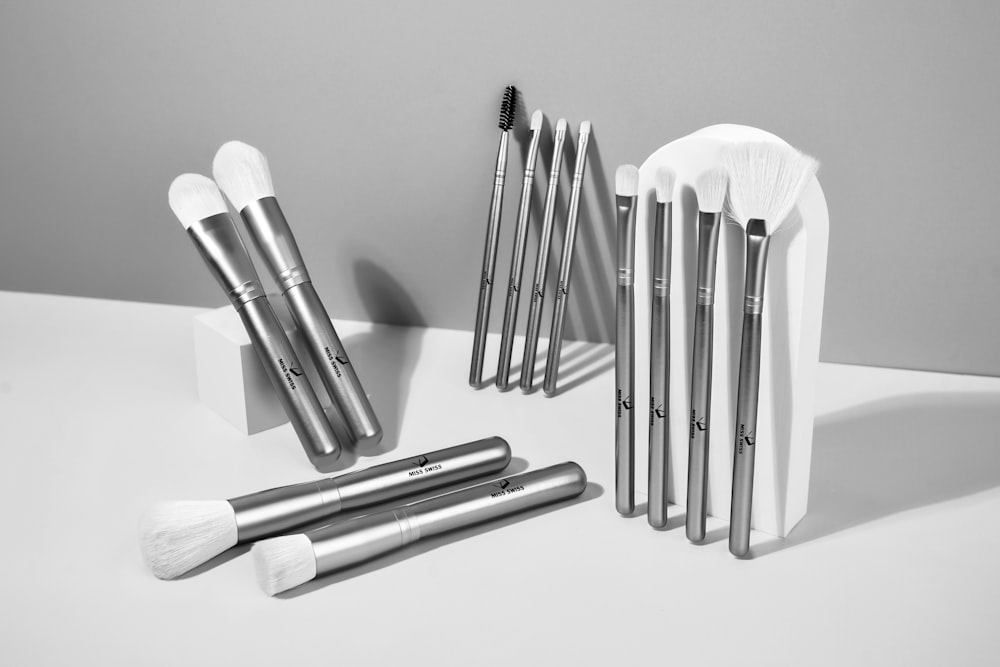 A collection of silver makeup brushes with white bristles are arranged on a white surface