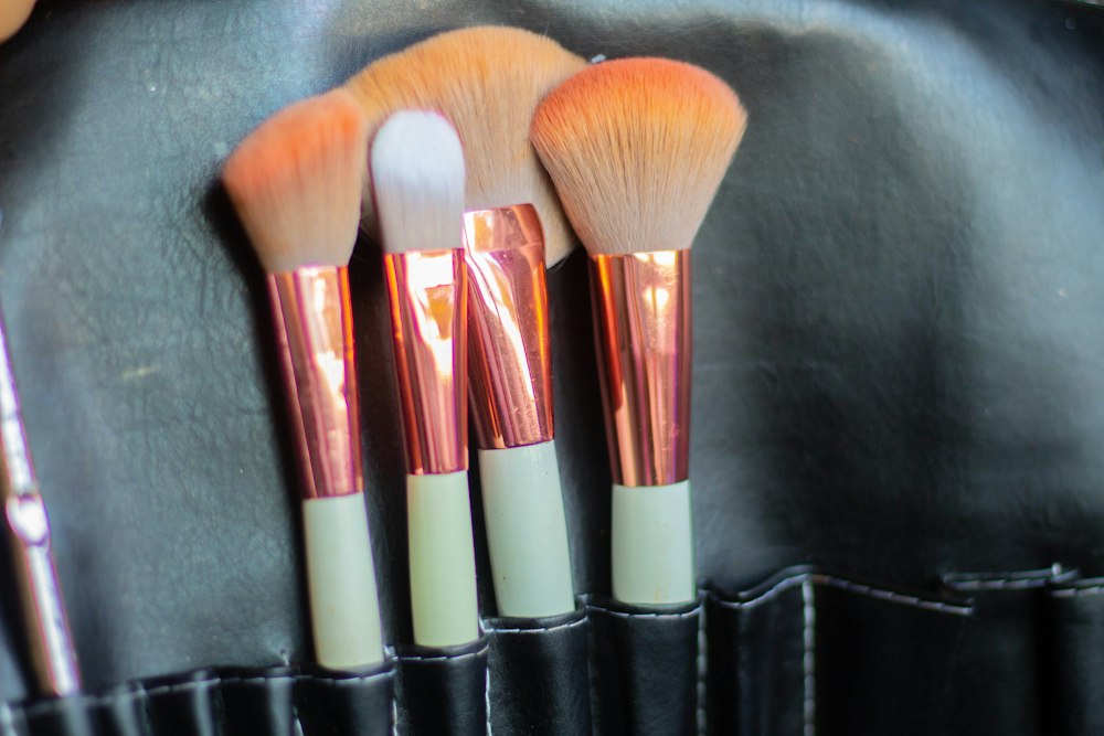 Four makeup brushes with copper ferrules and white handles rest in a black case