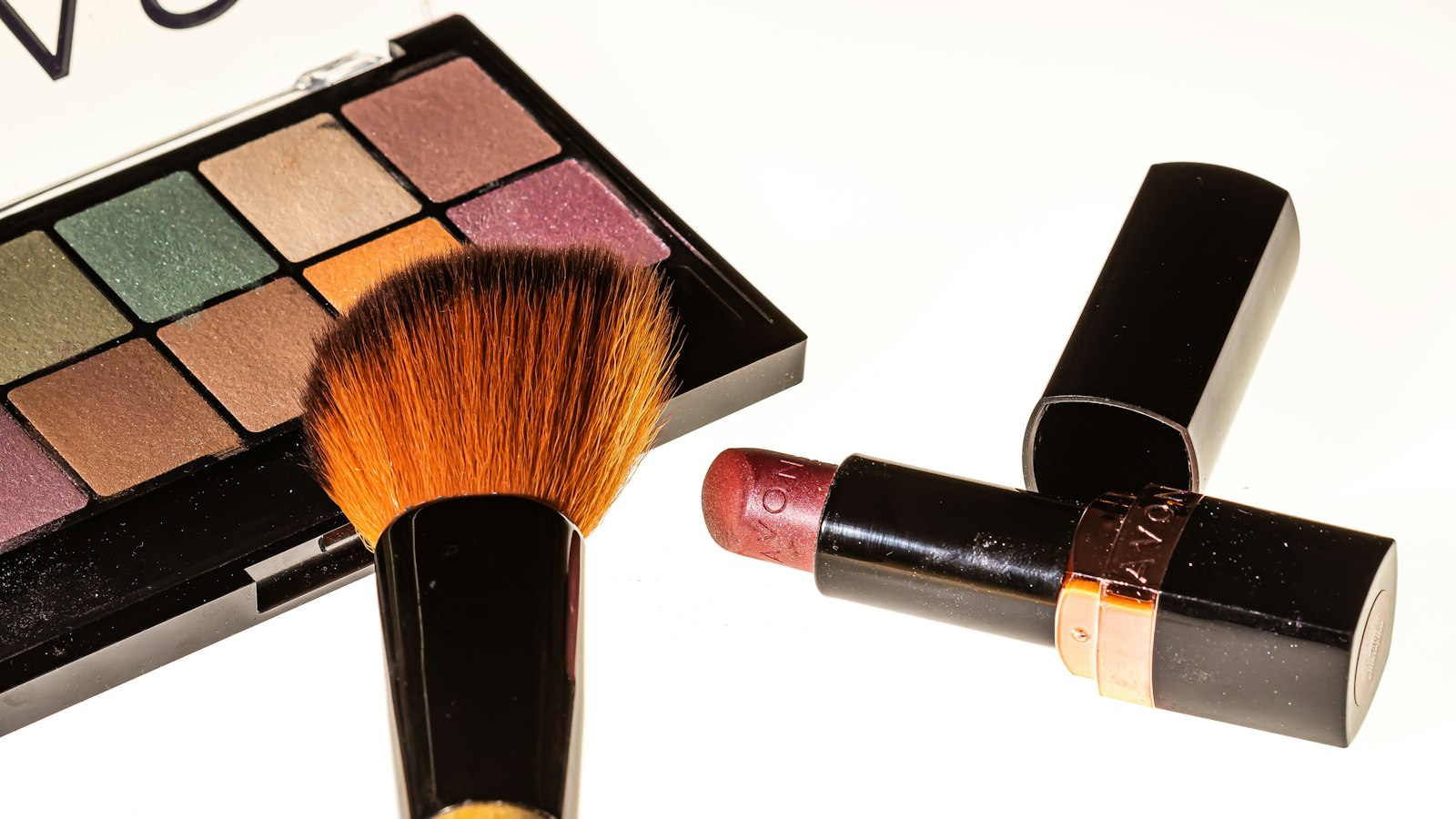 An open eyeshadow palette, a makeup brush, and an open tube of lipstick