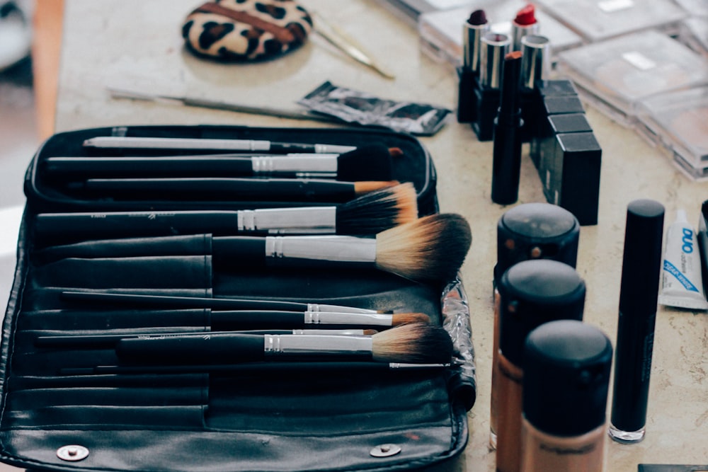 Makeup brushes in a black case alongside various cosmetics on a counter