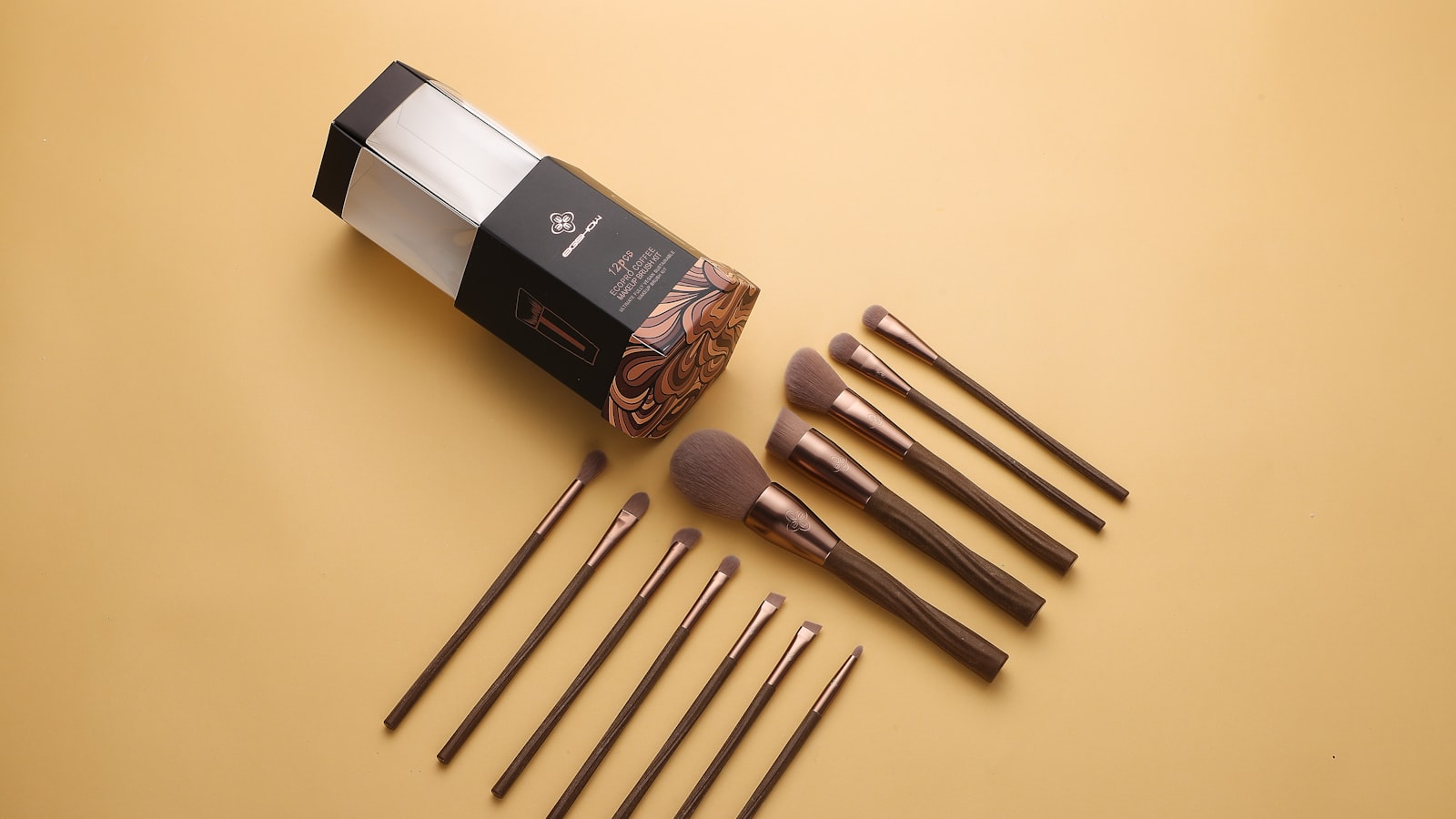 A cosmetic brush set with a box and ten brushes is laid out on a yellow surface
