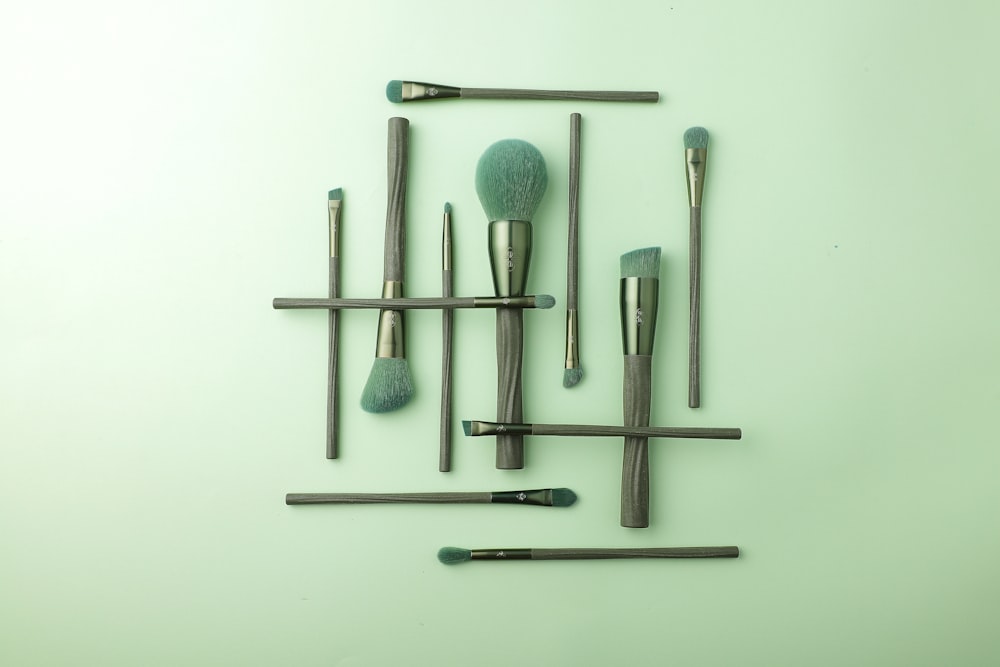 Green brushes with textured handles are arranged in a geometric pattern on a light green background