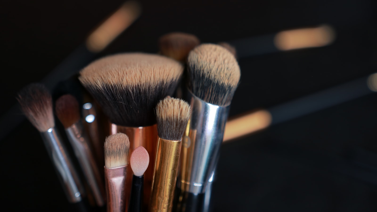 A bundle of various makeup brushes stands upright against a dark background